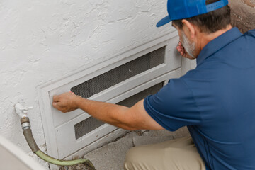 A home inspector is opening a crawl space access hatch underneath a residential home © Devka