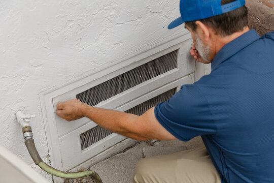 A home inspector is opening a crawl space access hatch underneath a residential home