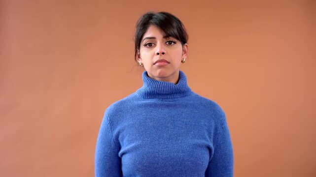 Woman shows expressions in blue sweater against brown background with change in mood and feeling throughout  