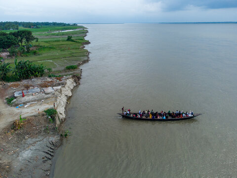 Chilmari, Bangladesh - 20 June 2025: Aerial view of a crowded wooden boat navigating the Brahmaputra river near the eroded banks and green fields.