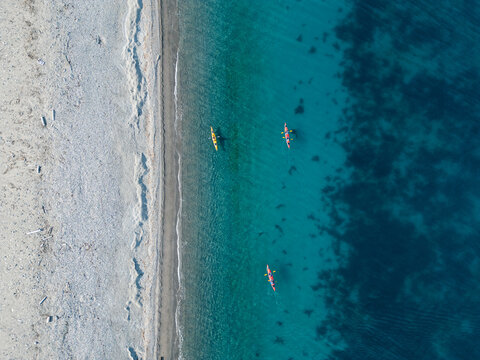 Svalbard and Jan Mayen - 29 June 2025: Aerial view of three kayaks with people paddling in turquoise water along a pebbly shoreline.