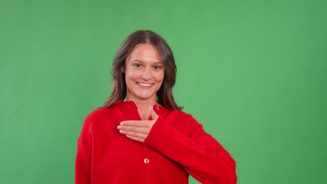 A woman in a red sweater pretending a smile and sadness against green background in simple setup