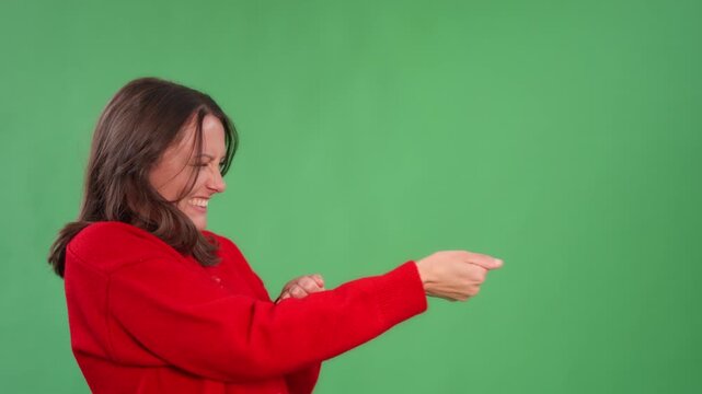 Woman performs hand gestures pretend to pull a rope in front of green screen during fun interaction in a studio setting on a bright day