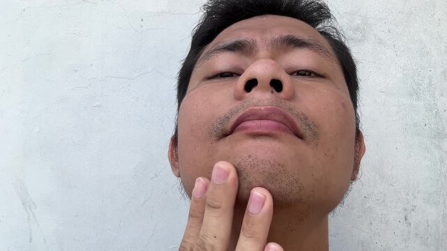 Asian man checking his facial stubble and skin texture