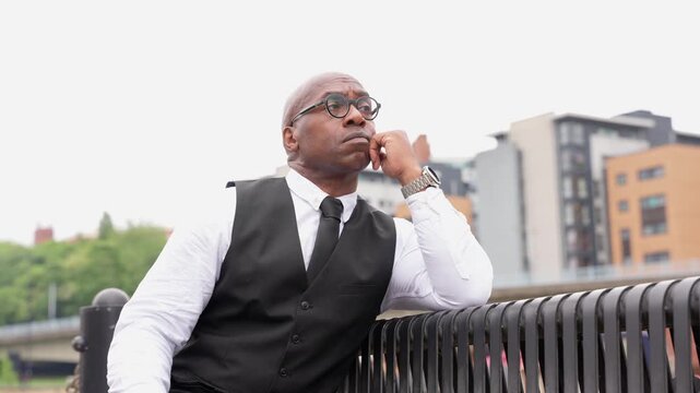 Man sits on bench in city, thinking deeply as buildings loom in background during overcast afternoon