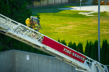 Firefighter in yellow turnout gear and yellow helmet with SCBA climbing aerial laddder with grass field in background.  © Daniel