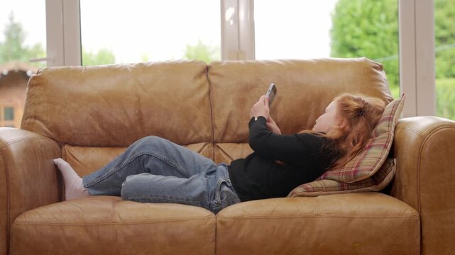 Child relaxes on sofa while watching phone in living room during afternoon hours