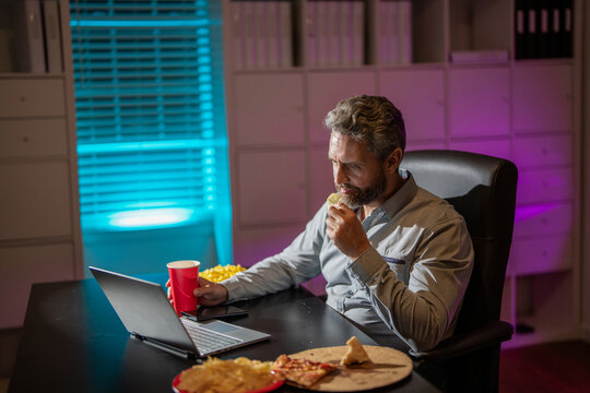 Freelancer eat pizza late at night. Night office with laptop and snack. Night office relaxation. Night job. Businessman eat snack while working on laptop. Busy employee office work during late night
