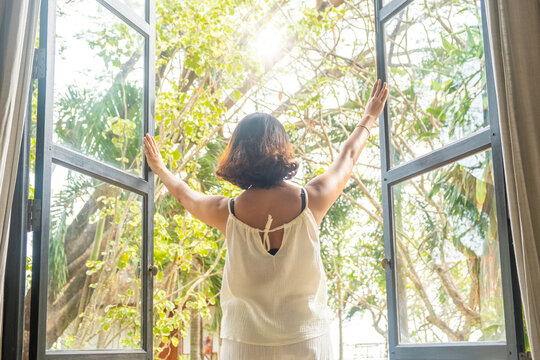 The woman was at the window in the bedroom. She opened the curtains on the window. In the morning and she looks at the view of mountains and trees at sunrise.	
