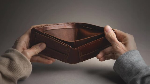 Empty brown leather wallet opened slowly showing no money inside with hands in natural light