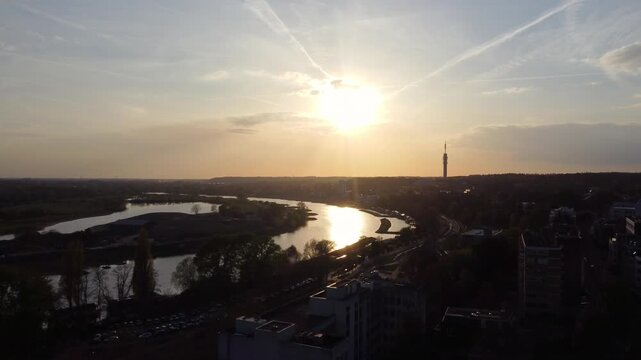 Nederrijn in Arnhem Gelderland Netherlands flows through Rhine delta floodplain with meanders, levees and urban edge reflecting sunset light as drone ascends revealing river system