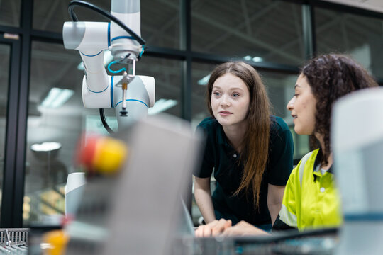 Engaged young woman student engineer in teamwork, learning about robot technology with robotic arm. Future education for industry automation and modern programming for machinery