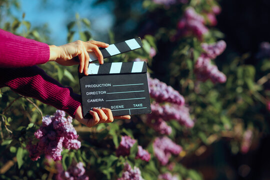 Hands Holding Cinema Clapperboard Outdoors In Front Of Blooming Lilacs. Director shooting video production outdoors in springtime blooming setting 