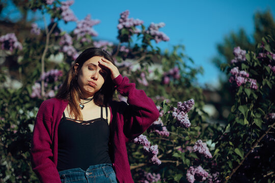 Stressed Woman Feeling Nauseated Near Lilacs Flowers. Overwhelmed female showing signs of pressure hot flashes during spring time