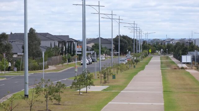 A straight residential street in Truganina with uniform grey rooftops, illustrating suburban car dependency and a lack of mature tree canopy in Melbourne's outer suburbs, Australia.