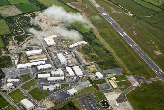 Waterford Regional Airport, Ireland - 02 July 2015: Aerial view of Waterford Airport featuring the runway, industrial hangars, and surrounding green fields under a light cloud cover.