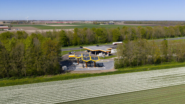 Bant, Netherlands - 21 April 2026: Aerial view of Fastned Charging Station with its solar roof, situated beside a highway and colorful tulip fields in the Dutch countryside.