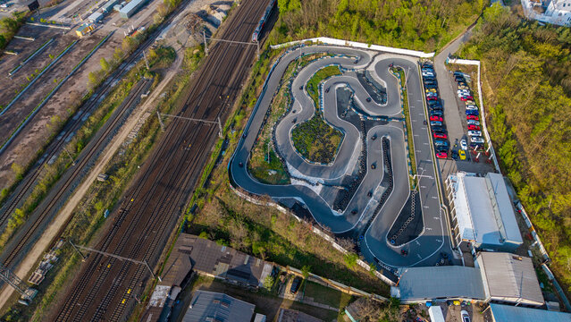 Prague, Czechia - 21 April 2026: Aerial view of KartPlanet go-kart track with winding asphalt lanes, adjacent railway tracks, and a parking area surrounded by lush green trees.