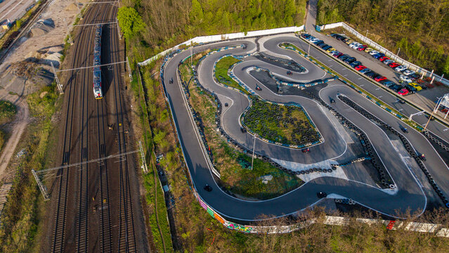 Prague, Czechia - 21 April 2026: Aerial view of the KartPlanet go-kart track with drivers racing on the circuit next to a train passing on parallel railway tracks and a parking lot filled with cars.