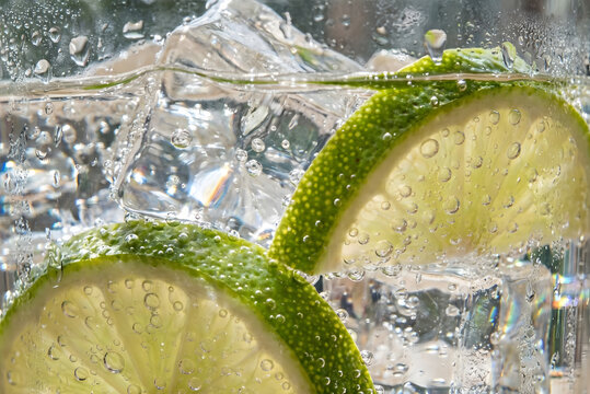 Extreme macro photography of fresh lime slices and crystal clear ice cubes in sparkling soda water with refreshing bubbles, summer drink concept.