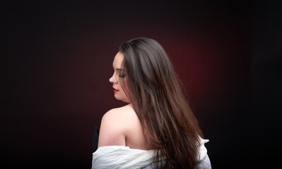 Fototapeta premium A young woman poses in a white lace blouse on a dark blue background. The shirt is unbuttoned and her beautiful breasts are visible.
