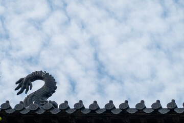 A traditional Chinese tiled roof featuring a mythical beast ornament stands silhouetted against a vast, clouded sky in a low-angle perspective.  © Yu