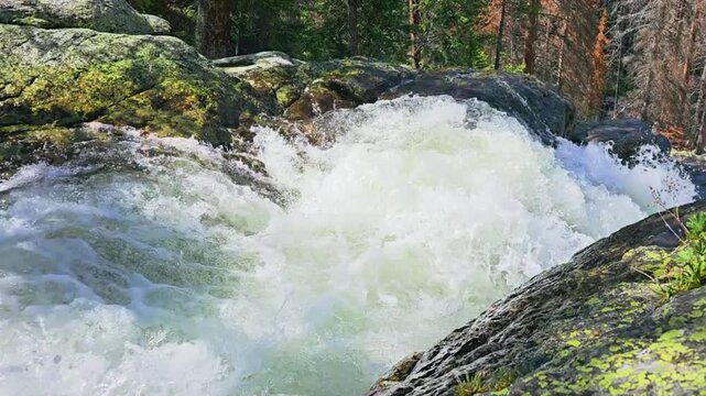 Wild river rapids cascading over granite rocks in a green forest, foamy whitewater rushing downstream through rugged wilderness, outdoor adventure and nature scenery.