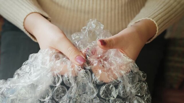 Woman hands popping air bubbles in plastic wrap to relieve stress.