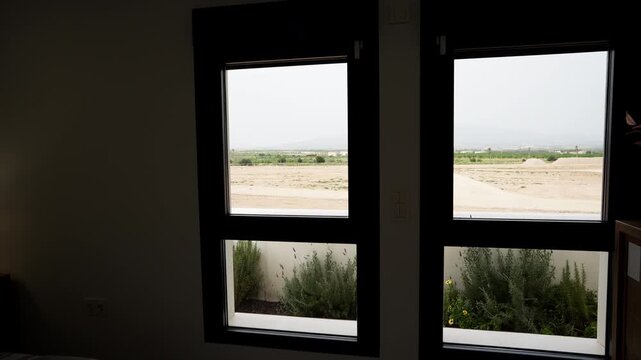 View through modern window frames overlooking open land and distant landscape. Minimal interior scene with natural light, framing concept, and calm residential perspective.