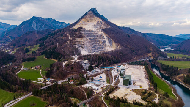 Klaus an der Pyhrnbahn, Austria - 23 March 2026: Aerial view of the VOEST Quarry on a steep mountainside with industrial facilities, surrounding forests, and the Steyr river under a cloudy sky.