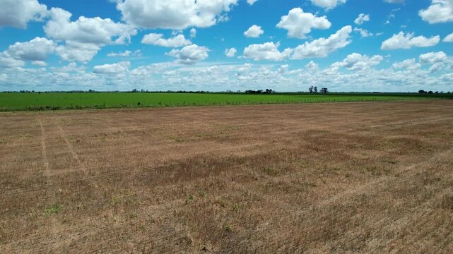 Drone flyover and rise vertically starting from dry brown harvested land to reveal a vast regional overview of fertile maize soybean and alfalfa plantations under a cloudy sky with cloud shadows in Ar