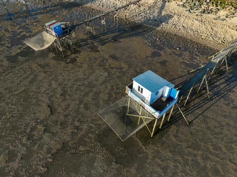 Yves, France - 22 September 2023: Aerial view of traditional fishing huts on stilts with large square nets over the muddy tidal flats during low tide.