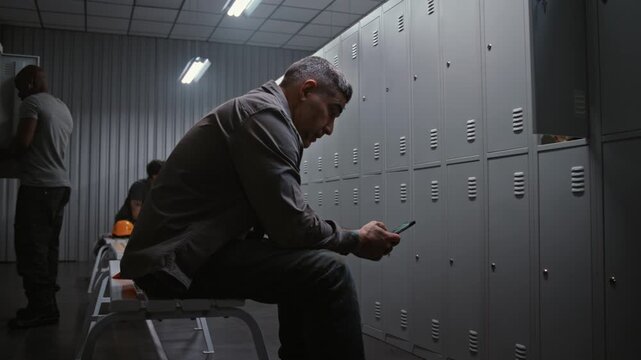 Managing Time And Schedule. Professional Industrial Worker Removes Safety Helmet, Checks Watch and Types Message on Smartphone in Modern Factory Dressing Room. Concept of Managing Time and Schedule.