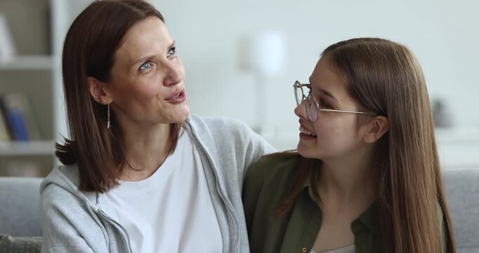 Closeup of loving mother talking to teen daughter, hugging, sitting on sofa at home, lead conversation, spend time together on leisure in living room. Family communication, friendly relationship, bond