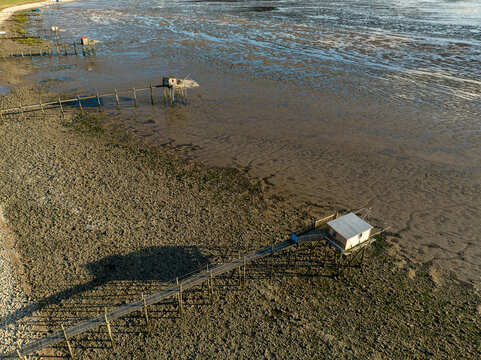 Yves, France - 22 September 2023: Aerial view of traditional fishing huts on stilts with long wooden walkways over the muddy coastline at low tide.