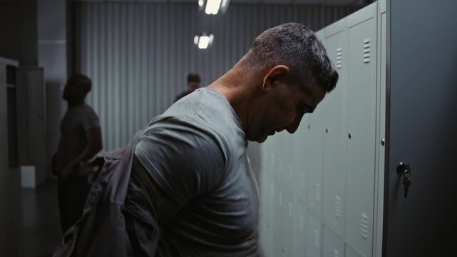 Group of Athletic Workers in Safety Helmets and Workwear Enjoy Lighthearted Conversation While Changing Clothes by Metal Lockers After Successful Manufacturing Day. Authentic Industrial Lifestyle.