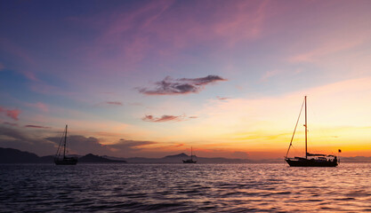 Koh Kradan sunrise with boats on water. Vibrant sky colors reflecting on calm sea. Silhouettes of boats anchored near tropical island. © Eugene Ga