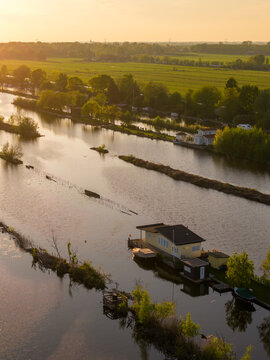 Breukelen, Netherlands - 25 April 2026: Aerial view of Scheendijk houseboats along narrow strips of land and waterways surrounded by lush green fields during golden hour.
