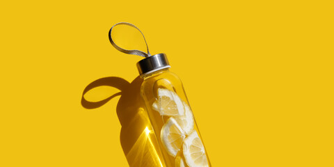 Lemon fruit water drink detox in bottle on yellow shadow at sunlight, banner. Selfcare, wellness, diet, healthy living concept. Glass reusable water bottle, eco friendly still life minimal aesthetics. © yrabota