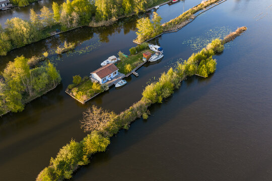 Breukelen, Netherlands - 25 April 2026: Aerial view of the Scheendijk recreational islands with a small cottage and moored boats surrounded by lush greenery and calm water.