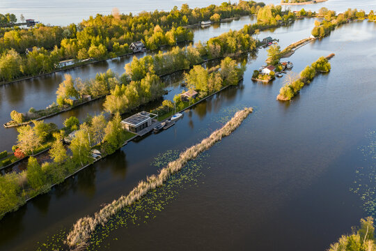 Breukelen, Netherlands - 25 April 2026: Aerial view of Scheendijk recreational islands with small cabins and lush green trees surrounded by calm water during golden hour.