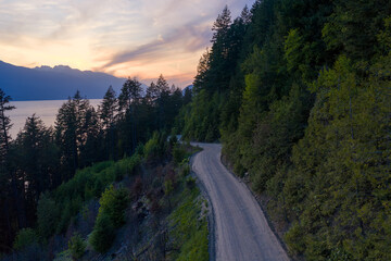 Obraz premium Winding Dirt Road Along Forested Hills Overlooking Lake at Sunset in British Columbia Canada