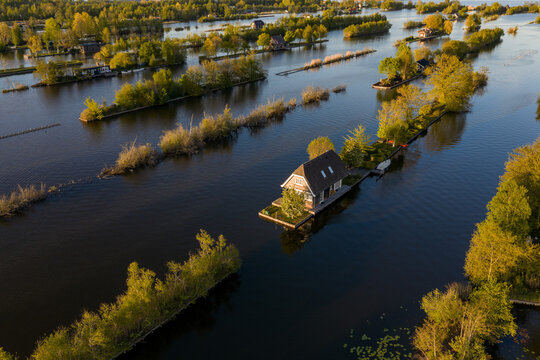Breukelen, Netherlands - 25 April 2026: Aerial view of Scheendijk recreational islands with small houses and lush green trees on the water during sunset.