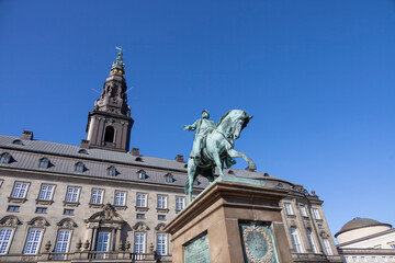 Naklejka premium The equestrian statue outside Christiansborg Palace, a historic site in Copenhagen, Denmark, framed by clear blue skies.
