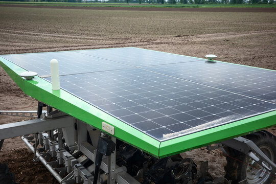 Autonomous mobile agricultural machine equipped with integrated solar panels operating across a rural farmland field during sustainable precision farming operations