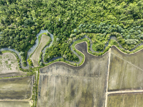 Aerial view of the winding river bordering the lush forest of Parco Naturale del Bosco delle Sorti della Partecipanza and agricultural fields in Trino, Piemonte, Italy.