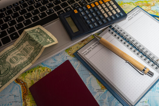 Travel planning concept with passport, calculator, one dollar bill, notebook and pen placed on a world map symbolizing vacation budgeting, travel preparation, costs and time management