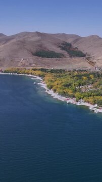 Vertical drone view of Lake Sevan shoreline with autumn forest and hills, Armenia