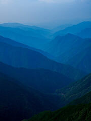 Naklejka premium 夜明け。雄大な山岳地帯の風景。山の稜線。朝もや。ガス。霧。高山の森林がレイヤーのように折り重なる景色。自然風景。遠近感。空気遠近法のサンプル。縦構図