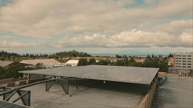 Expansive photovoltaic structure providing clean power for hydrogen testbed covering university parking garage looking toward ocean horizon beneath cloudy sky captured via slow reversing drone